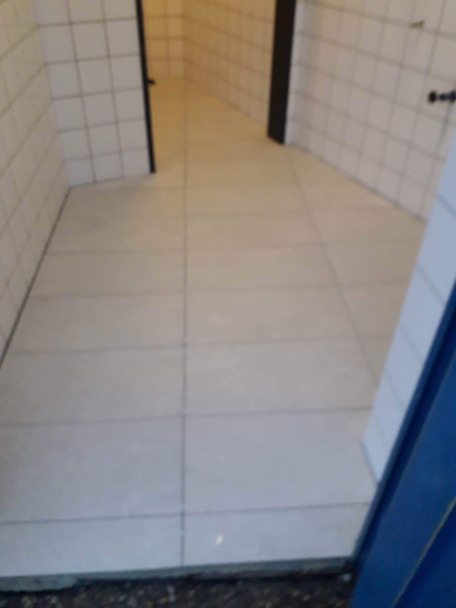 Świeżo położone, jasnoszare płytki podłogowe w korytarzu z białymi, kwadratowymi płytkami na ścianach i czarnymi ościeżnicami drzwi.