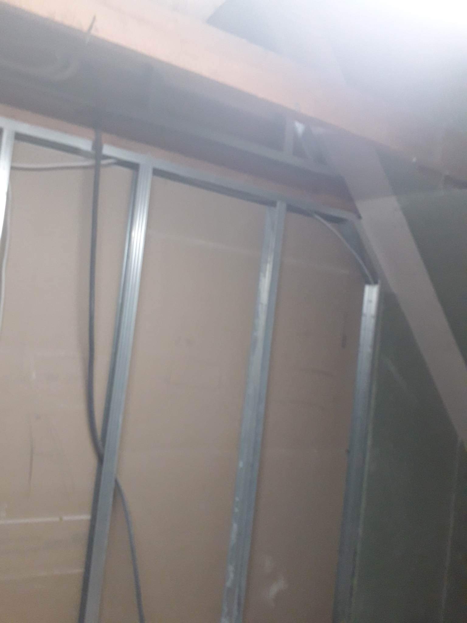 Stelaż z profili metalowych i płyty gipsowo-kartonowej w trakcie montażu, widoczne przewody elektryczne, surowy stan wnętrza.