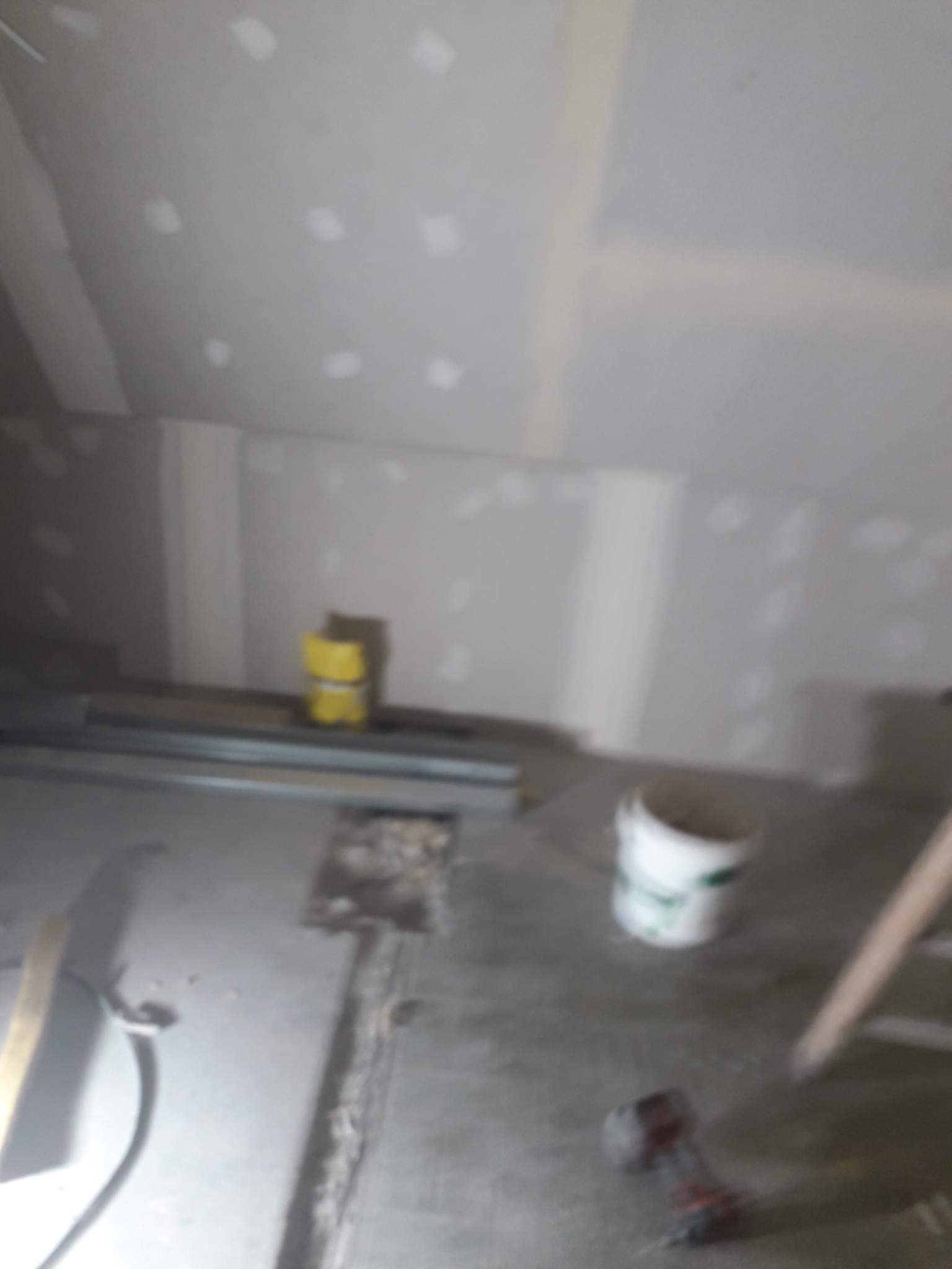 Wnętrze w trakcie prac wykończeniowych: sufit i ściany z płyt gipsowo-kartonowych, widoczne szpachlowanie, narzędzia pracy i wiadro farby na podłodze.