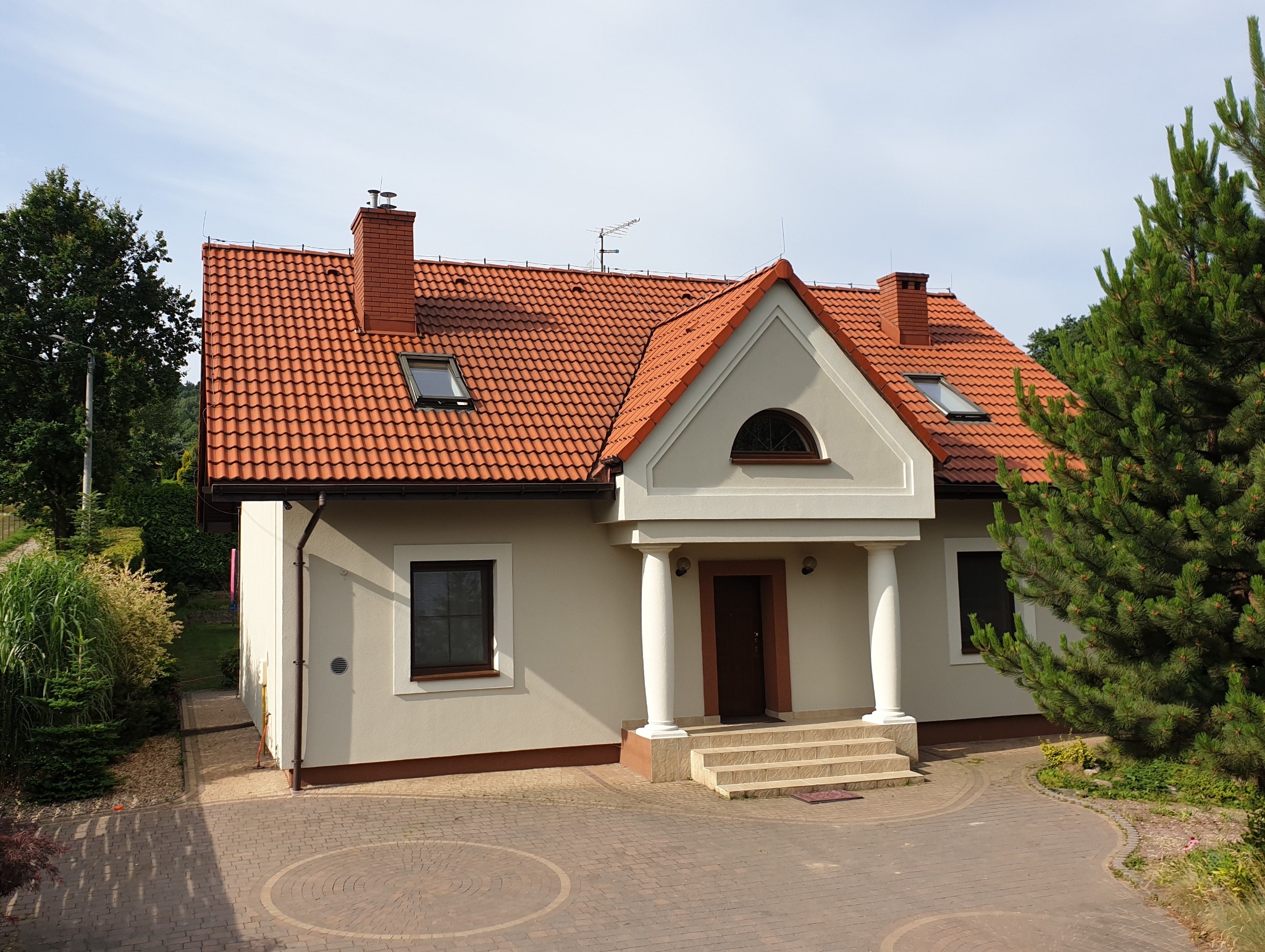 Dwupiętrowy dom z czerwonym dachem z dachówki, białymi ścianami i kolumnami przy wejściu, widoczny z góry