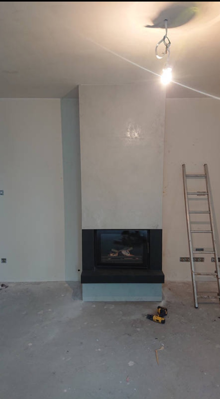 Nowoczesny, czarny wkład w obudowie z szarego betonu architektonicznego, drabina i narzędzia na podłodze w trakcie montażu.