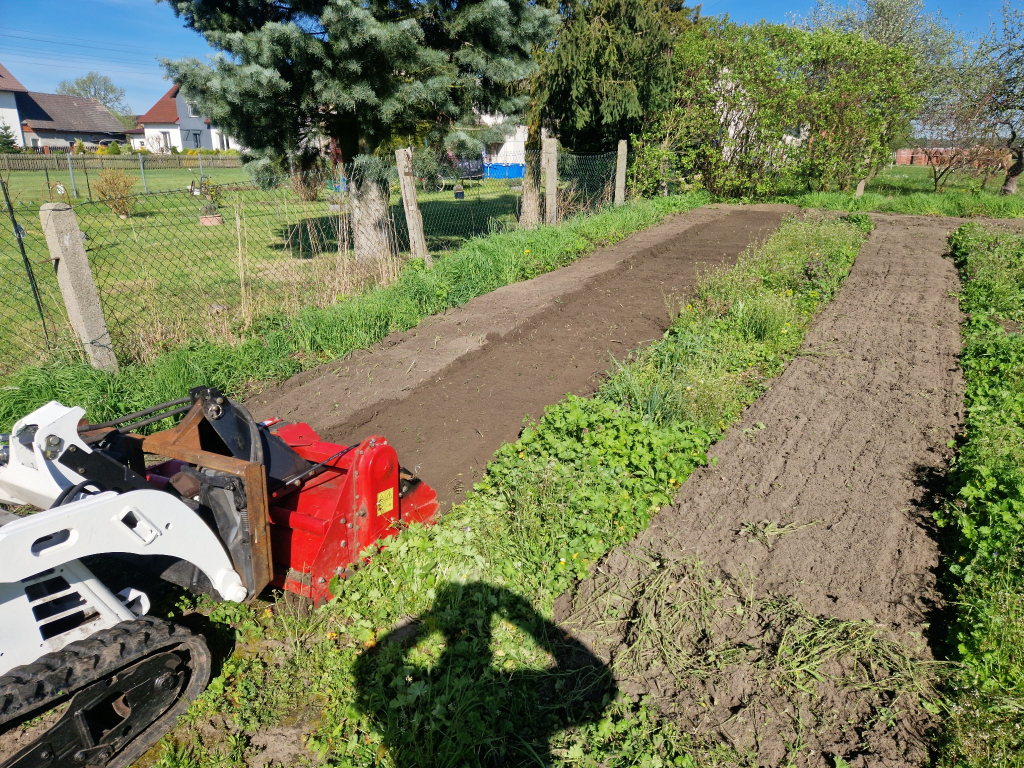 Przygotowany pod uprawę, spulchniony glebogryzarką teren w ogrodzie, widoczny cień osoby fotografującej.