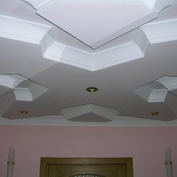 3D HOUSE - Biały, profilowany sufit podwieszany z geometrycznymi zdobieniami i punktowymi lampami, widok z dołu na fragment ściany w kolorze pudrowego różu.