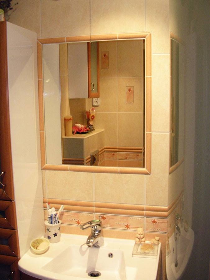 Umywalka z baterią i akcesoriami łazienkowymi, widok w lustrze odbija fragment blatu i szafki z dekoracjami, beżowe płytki z motywem gwiazdek na ścianach.