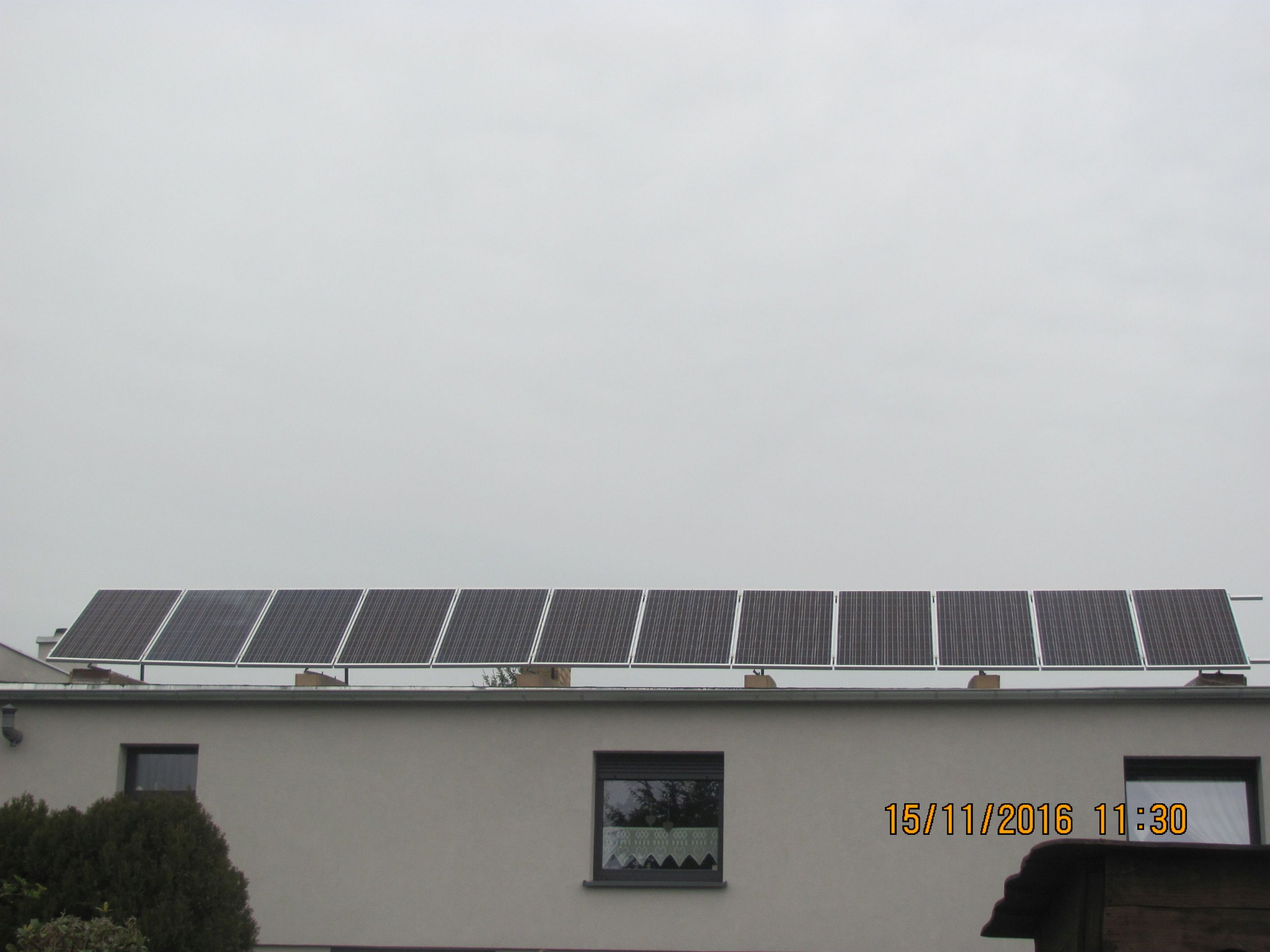 Rząd paneli słonecznych zamontowanych na dachu budynku, widocznych z dołu, z datą i godziną w prawym dolnym rogu.