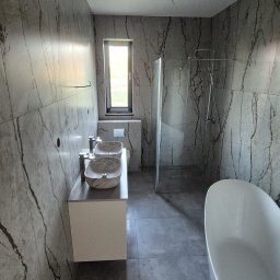 Remonty Adrian Stypuła - Nowoczesna łazienka z płytkami imitującymi marmur, owalną wanną i dwiema umywalkami w kształcie mis na blacie. Minimalistyczny design, szklana kabina prysznicowa.