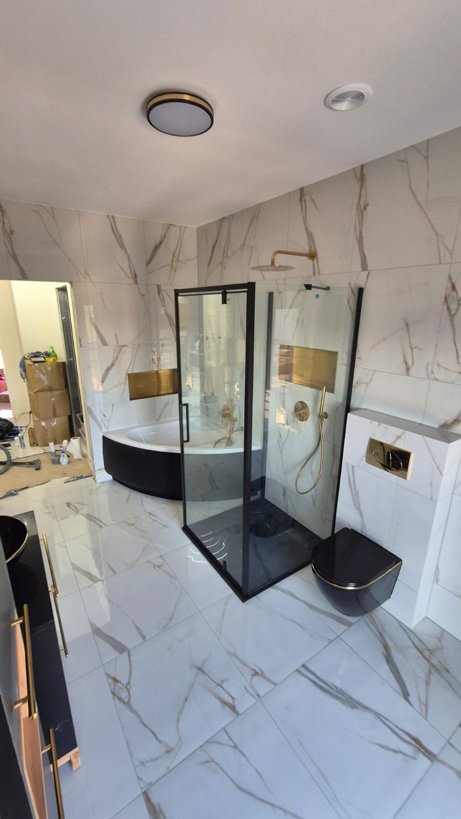 Nowoczesna łazienka z kabiną prysznicową typu walk-in, marmurowe płytki, czarna armatura z elementami złota, oświetlenie sufitowe.