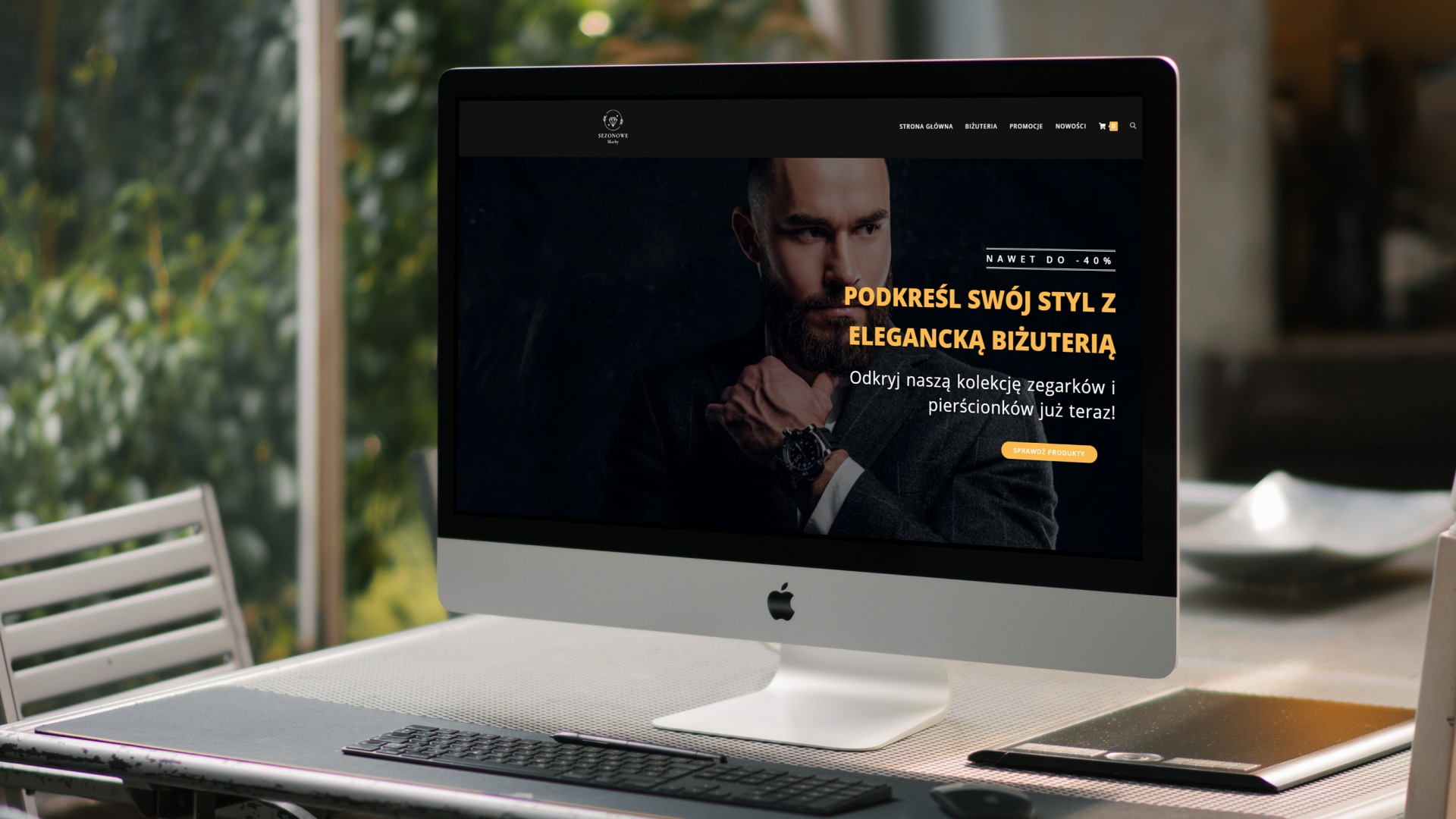 Ekran komputera iMac prezentuje stronę internetową sklepu z biżuterią, na pierwszym planie klawiatura i tablet graficzny na metalowym stole.