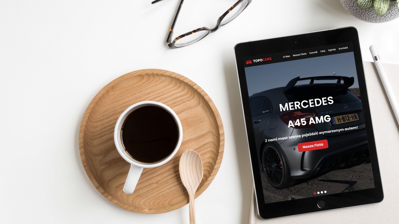 Tablet wyświetla stronę internetową z samochodem Mercedes A45 AMG, obok filiżanka kawy na drewnianej tacy, okulary i ołówek na białym tle.