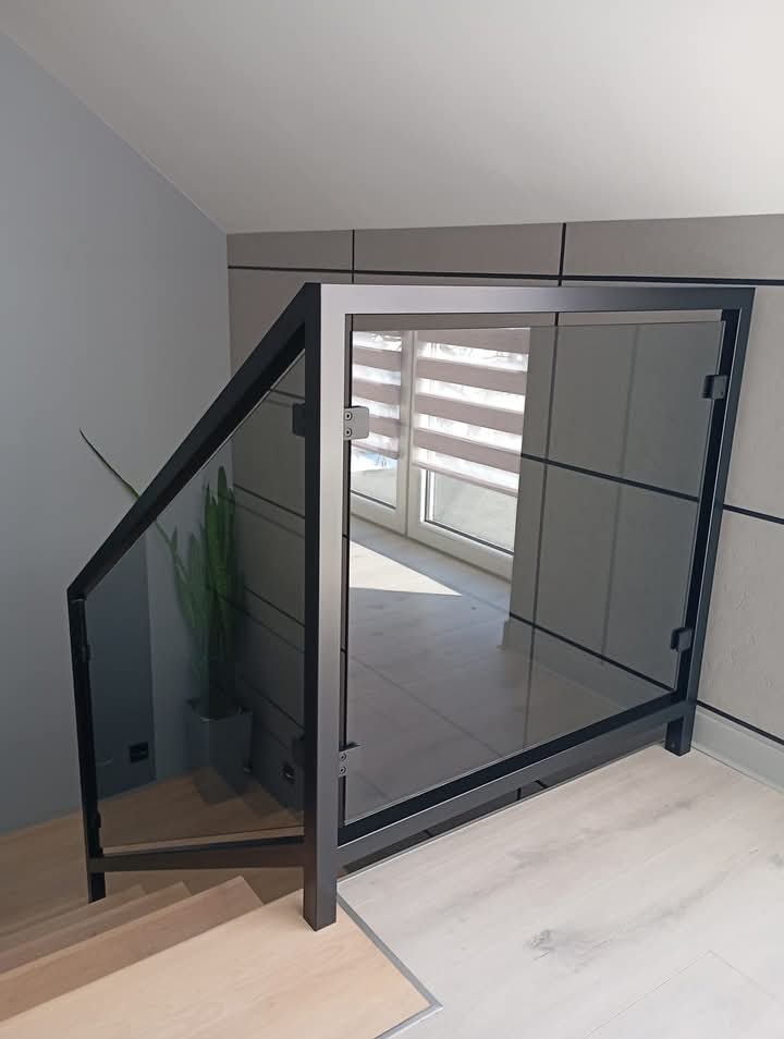 Szklana balustrada schodowa z czarną ramą, widok z dołu na schody i okno z żaluzjami w tle.