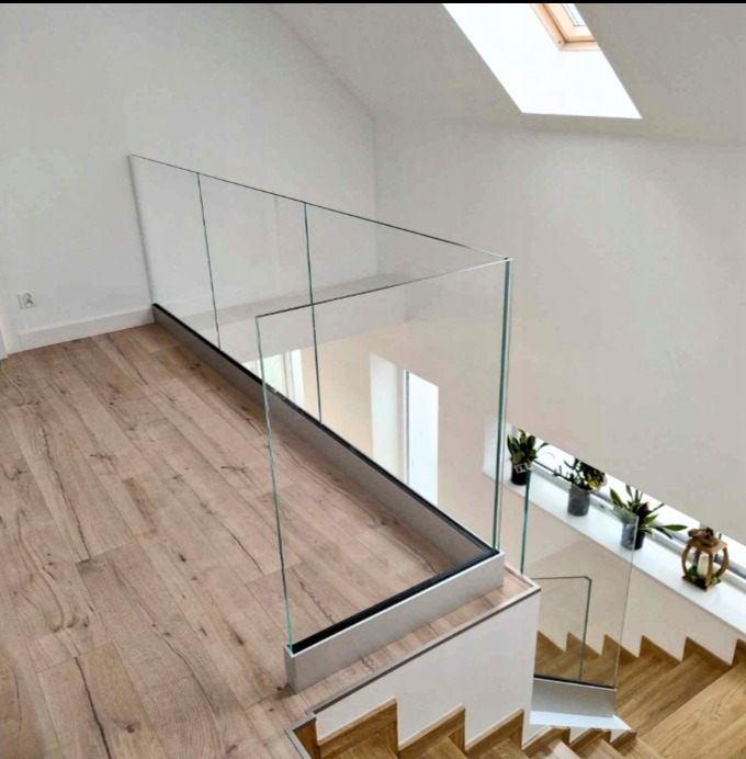 Szklana balustrada z metalowym profilem w nowoczesnym wnętrzu, widok z góry na schody z drewnianymi stopniami.
