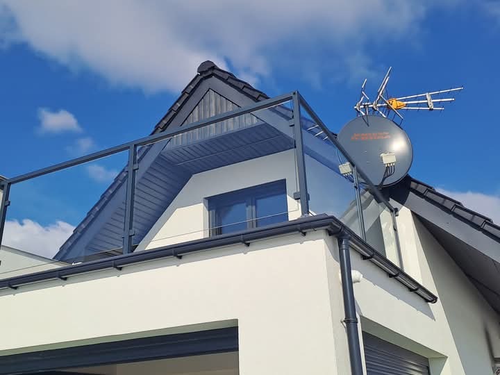 Szklana balustrada z metalową ramą na balkonie nowoczesnego domu z anteną satelitarną na dachu w słoneczny dzień.