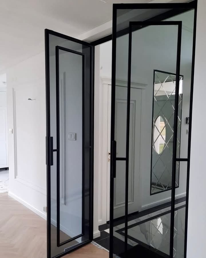 Czarne, przeszklone drzwi dwuskrzydłowe w stylu loftowym, z widocznymi refleksami światła na szkle i czarną podłogą w geometryczny wzór.