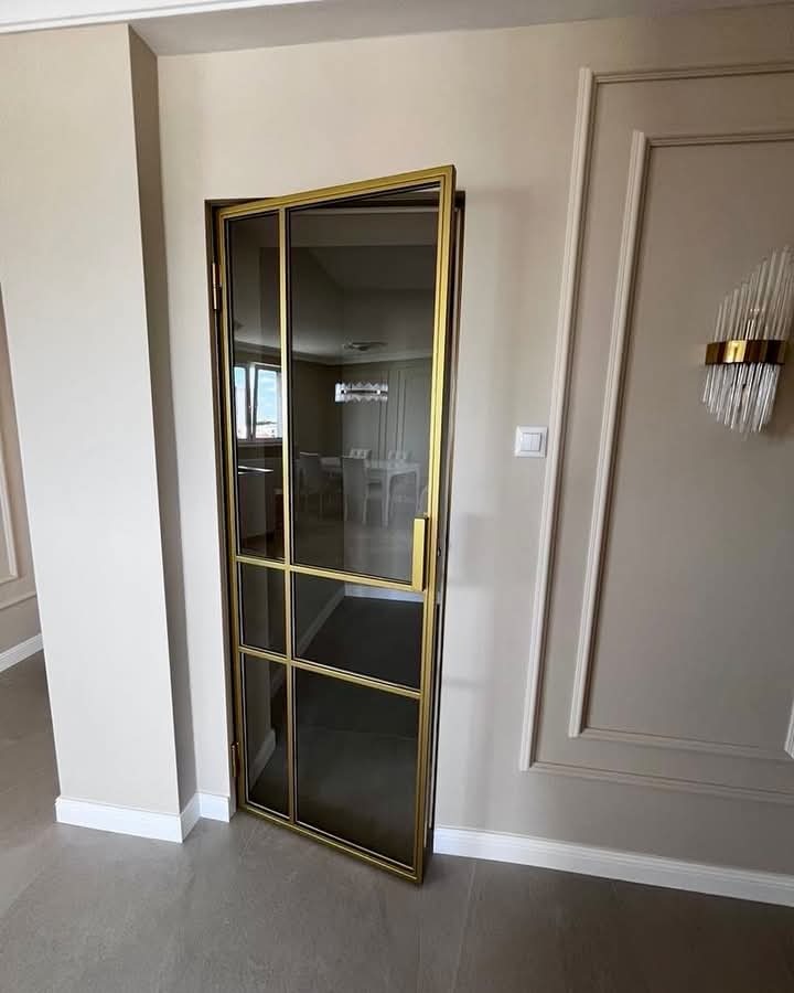 Otwarta, szklana ścianka działowa z złotymi profilami, oddzielająca pomieszczenia w nowoczesnym wnętrzu.