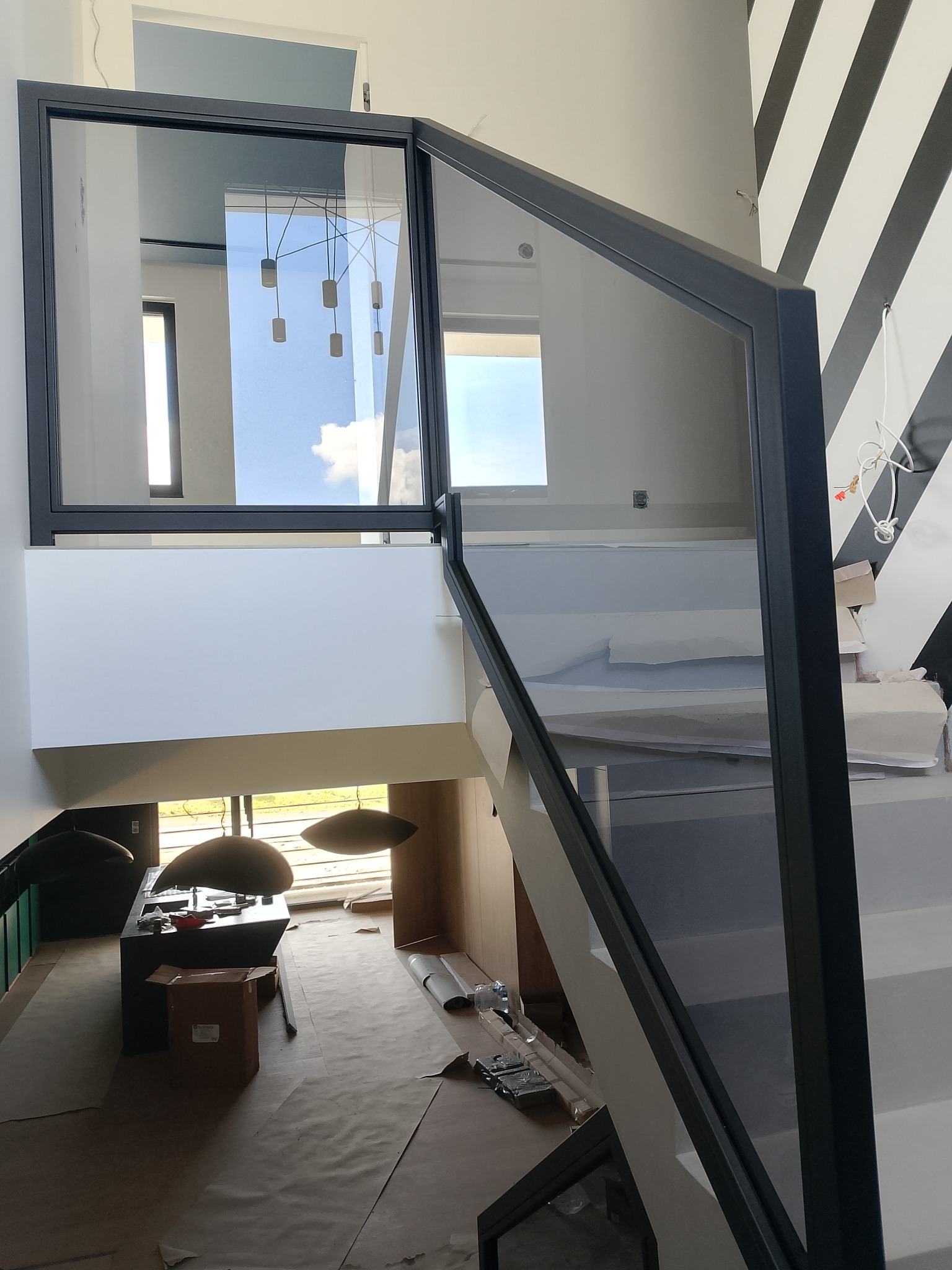 Nowoczesna balustrada szklana z czarną ramą, widok z góry na schody i wnętrze domu, z elementami dekoracyjnymi na ścianie. Estetyczne i minimalistyczne wykończenie.