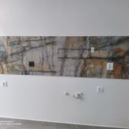 Ściana z fragmentem dekoracyjnej płyty imitującej kamień, nad gniazdkami elektrycznymi, widoczne kable wystające ze ściany, szpachlowane ślady po instalacji.