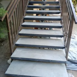 Betonowe schody zewnętrzne z metalową balustradą, widok z dołu, częściowo przykryte folią ochronną.