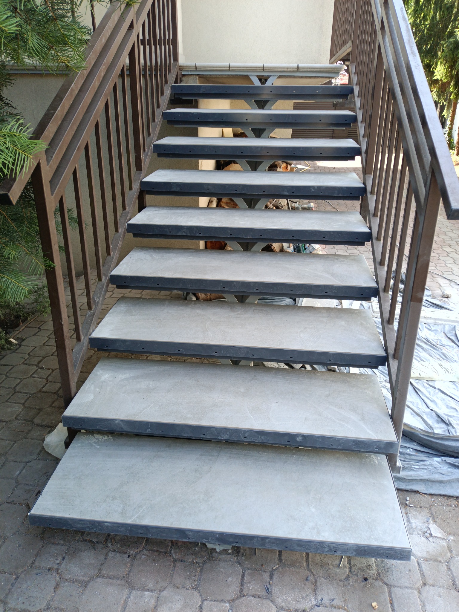 Betonowe schody zewnętrzne z metalową balustradą, widok z dołu, częściowo przykryte folią ochronną.