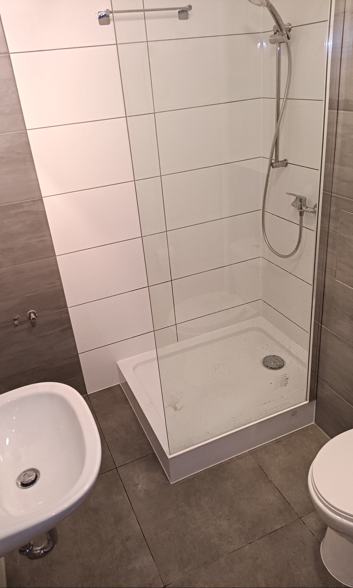 Nowoczesna łazienka z kabiną prysznicową ze szklanymi ściankami, białą umywalką i szarą glazurą.