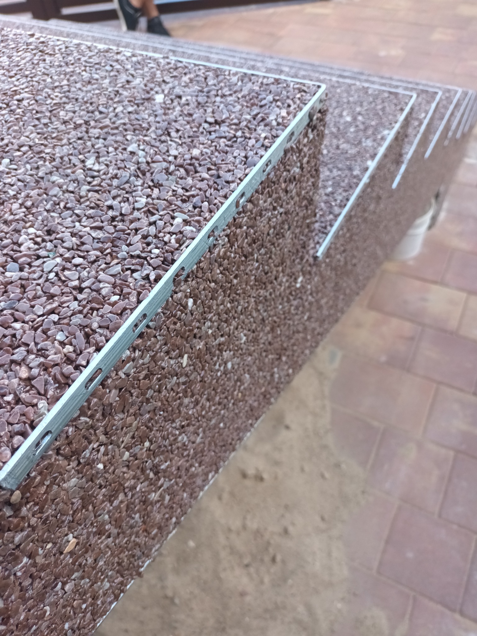 Schody zewnętrzne wykończone brązowym kamieniem otoczakowym, z metalową listwą krawędziową, widoczne z bliska pod kątem.