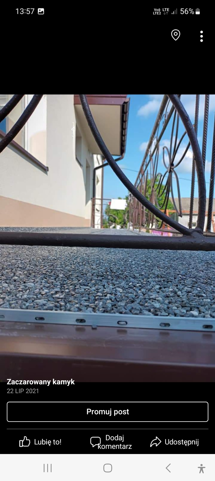 Powierzchnia tarasu wykończona drobnymi kamykami, widok z niskiej perspektywy, z fragmentem metalowej balustrady i elewacji budynku w tle.