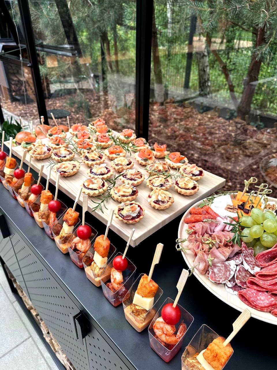 Elegancki catering: Mini tartaletki z łososiem i konfiturą, przekąski na szpadkach z krewetkami, serem i pomidorkami koktajlowymi w małych pojemnikach oraz talerz wędlin i serów z winogronami...