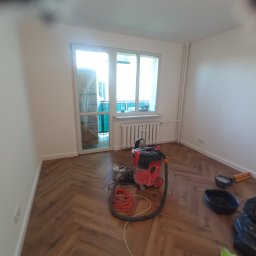 P.W.W.R. PROFESSIONAL Robert Borkowski - Pokój po ułożeniu paneli podłogowych w jodełkę, widoczny odkurzacz przemysłowy, narzędzia i resztki materiałów budowlanych.