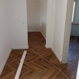 P.W.W.R. PROFESSIONAL Robert Borkowski - Układanie paneli w jodełkę w korytarzu w Głogowie, widoczne listwy przypodłogowe i fragment paczki paneli Vega.