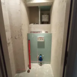 Łazienka w trakcie prac: widoczne surowe ściany, zamontowana płyta karton-gips z instalacją podtynkową WC, poziomica laserowa wyznaczająca linie, poziomica pionowa oparta o ścianę.