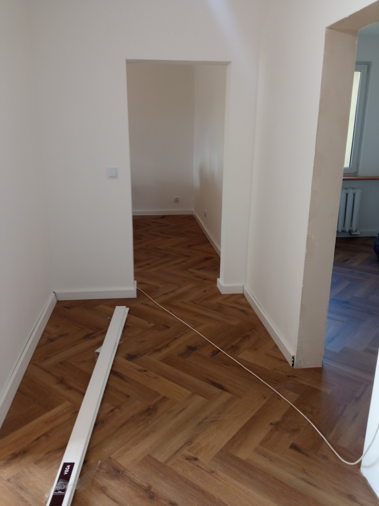 Układanie paneli w jodełkę w korytarzu w Głogowie, widoczne listwy przypodłogowe i fragment paczki paneli Vega.