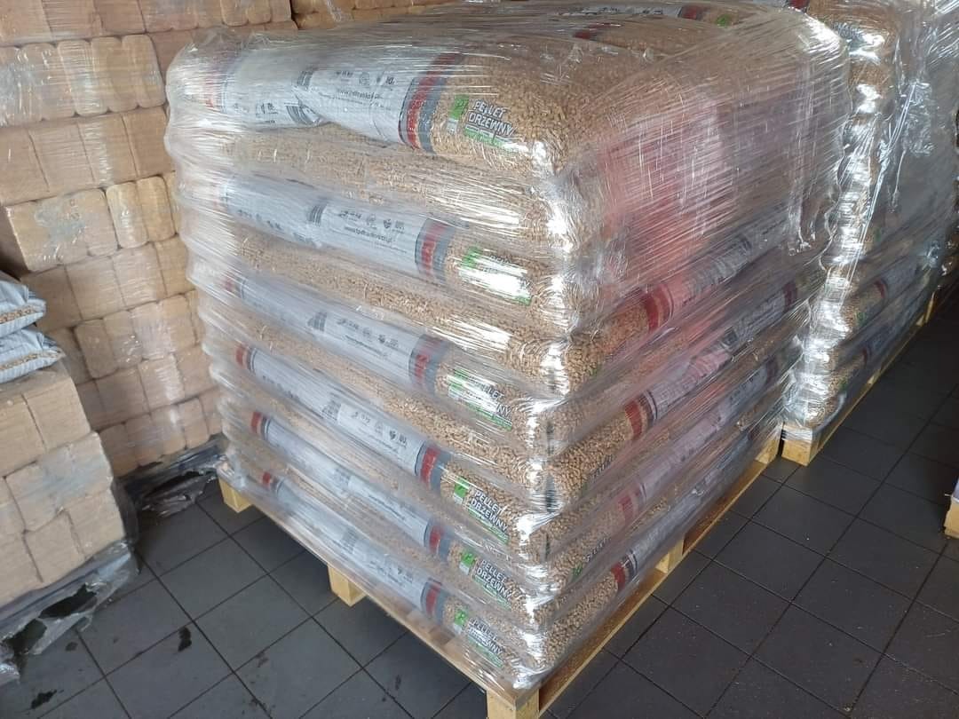 Paleta z workami z granulatem drzewnym, owinięta folią stretch, składowana w magazynie, widoczne etykiety z nazwą produktu.