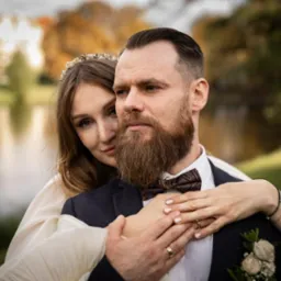 Para młoda w objęciach na tle parku z jeziorem, panna młoda z delikatną ozdobą we włosach, pan młody w muszce z wzorem paisley.