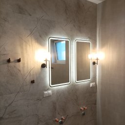 MWAInstal - Nowoczesna łazienka z dwoma podświetlanymi lustrami i kinkietami na marmurowej ścianie. Widoczne włączniki i instalacja wodna.
