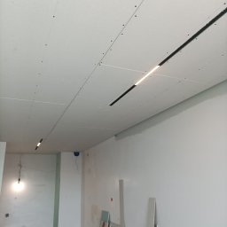 MWAInstal - Sufit podwieszany z zamontowanym oświetleniem liniowym LED. Widoczne płyty gipsowo-kartonowe i elementy konstrukcyjne. W tle ściany w trakcie wykończenia.