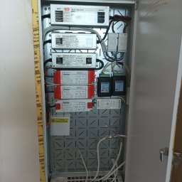 MWAInstal - Otwarta szafka elektryczna z zamontowanymi zasilaczami LED, sterownikami i okablowaniem. Widoczne elementy instalacji oświetleniowej wewnątrz metalowej obudowy.