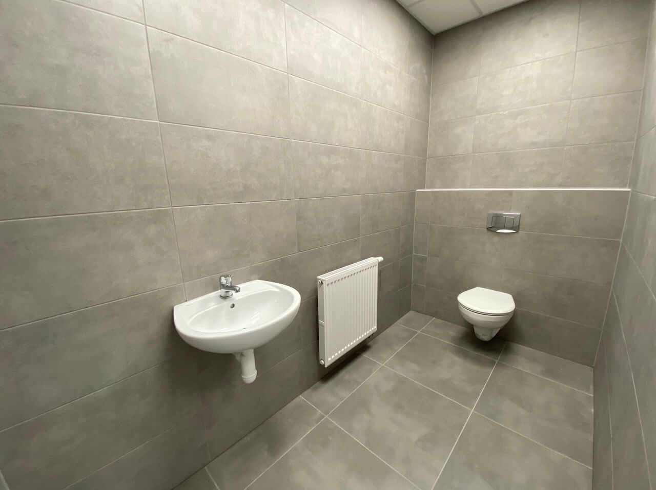 Wykończona łazienka w odcieniach szarości z umywalką, grzejnikiem drabinkowym i podwieszaną toaletą.