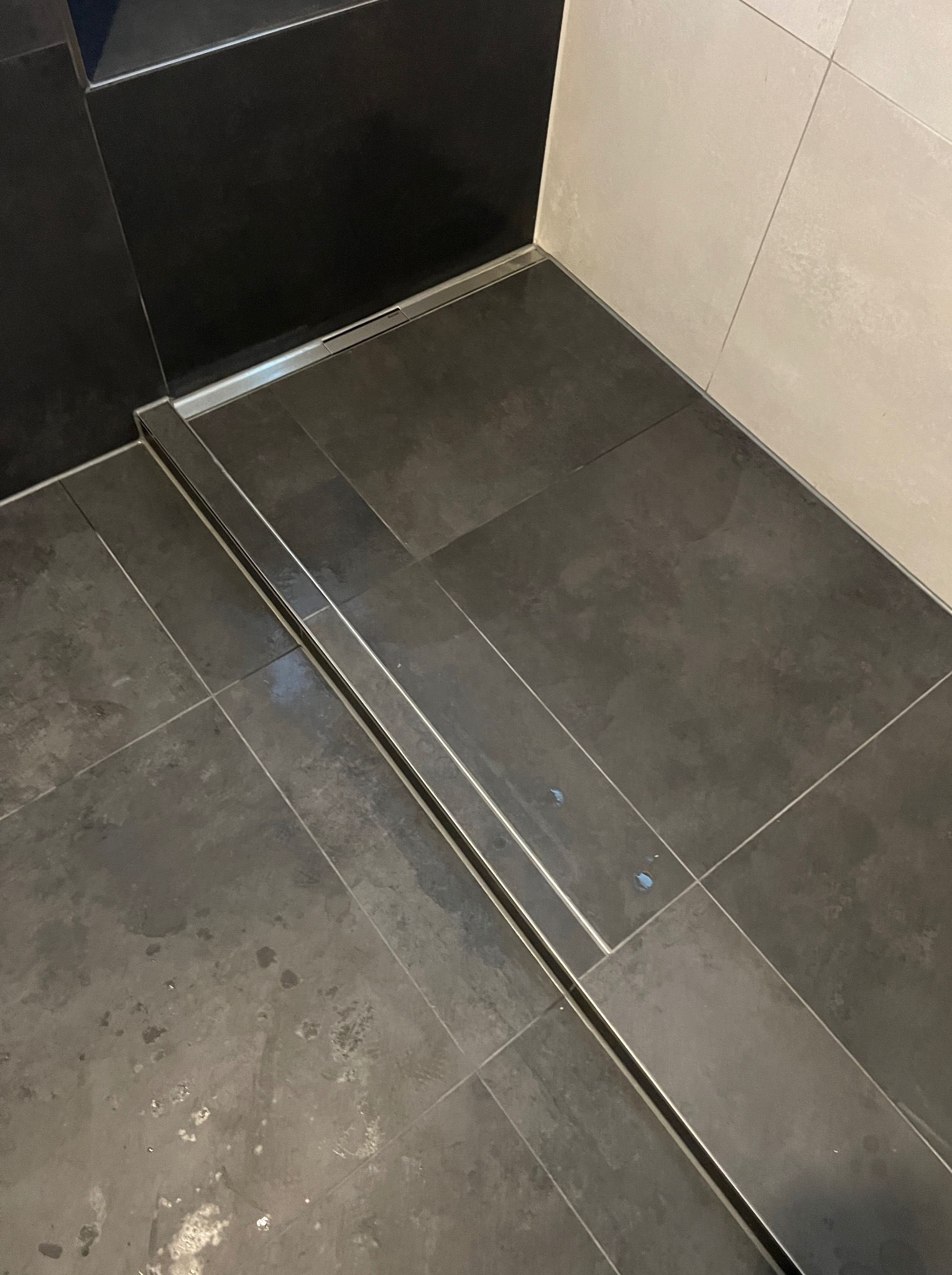 Czarno-biała łazienka z odpływem liniowym, widok z góry na szare płytki podłogowe i białe płytki ścienne.