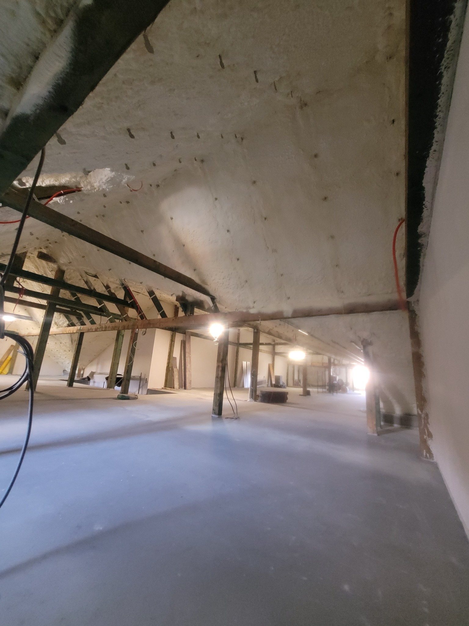 Ocieplone poddasze pianką PUR z widoczną konstrukcją drewnianą i instalacją elektryczną. Widok na przestrzeń poddasza z oświetleniem.