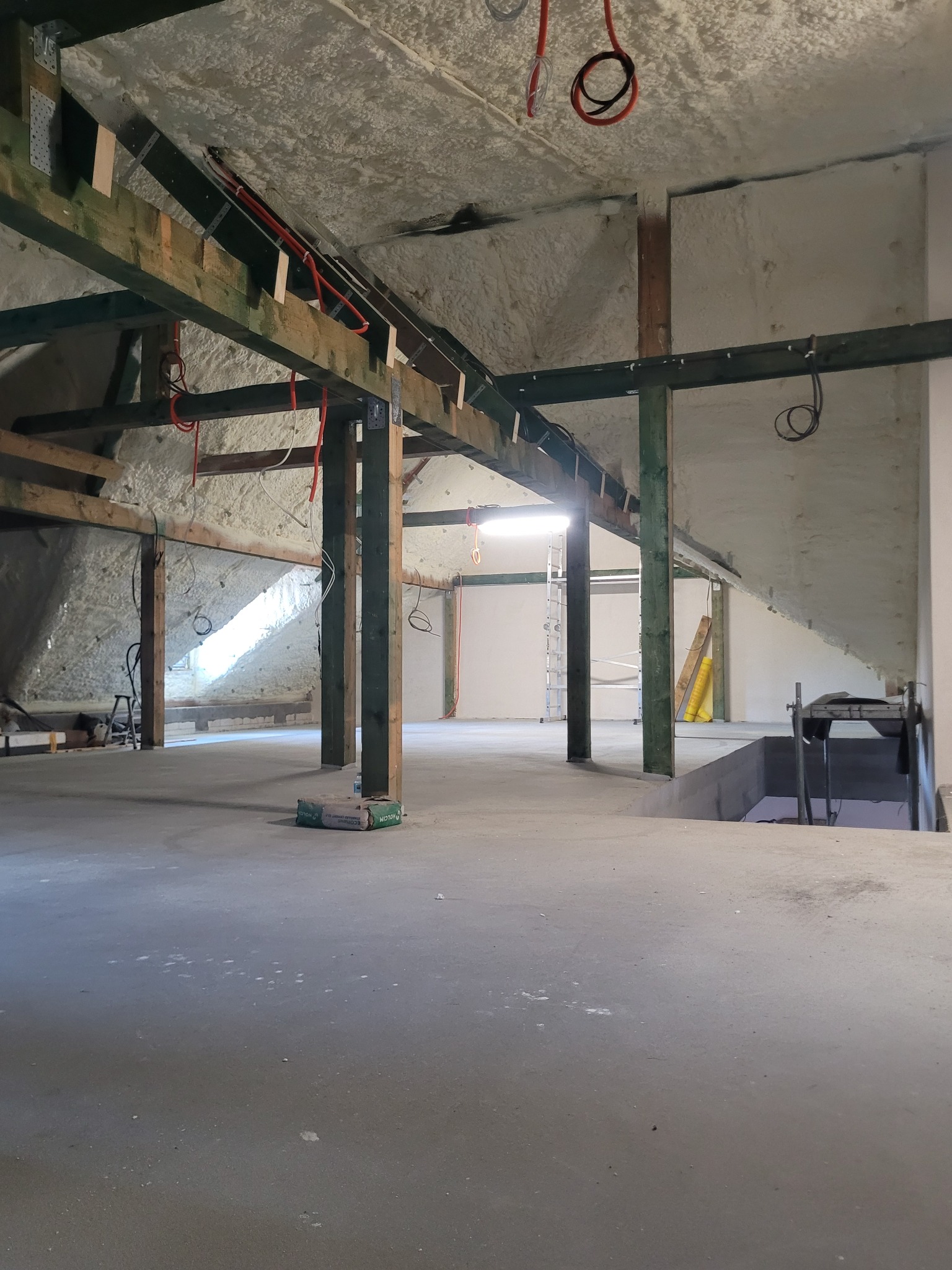 Poddasze po natrysku izolacji pianką, widoczne drewniane elementy konstrukcyjne i instalacje elektryczne. Izolacja pokrywa skośne ściany i sufit.