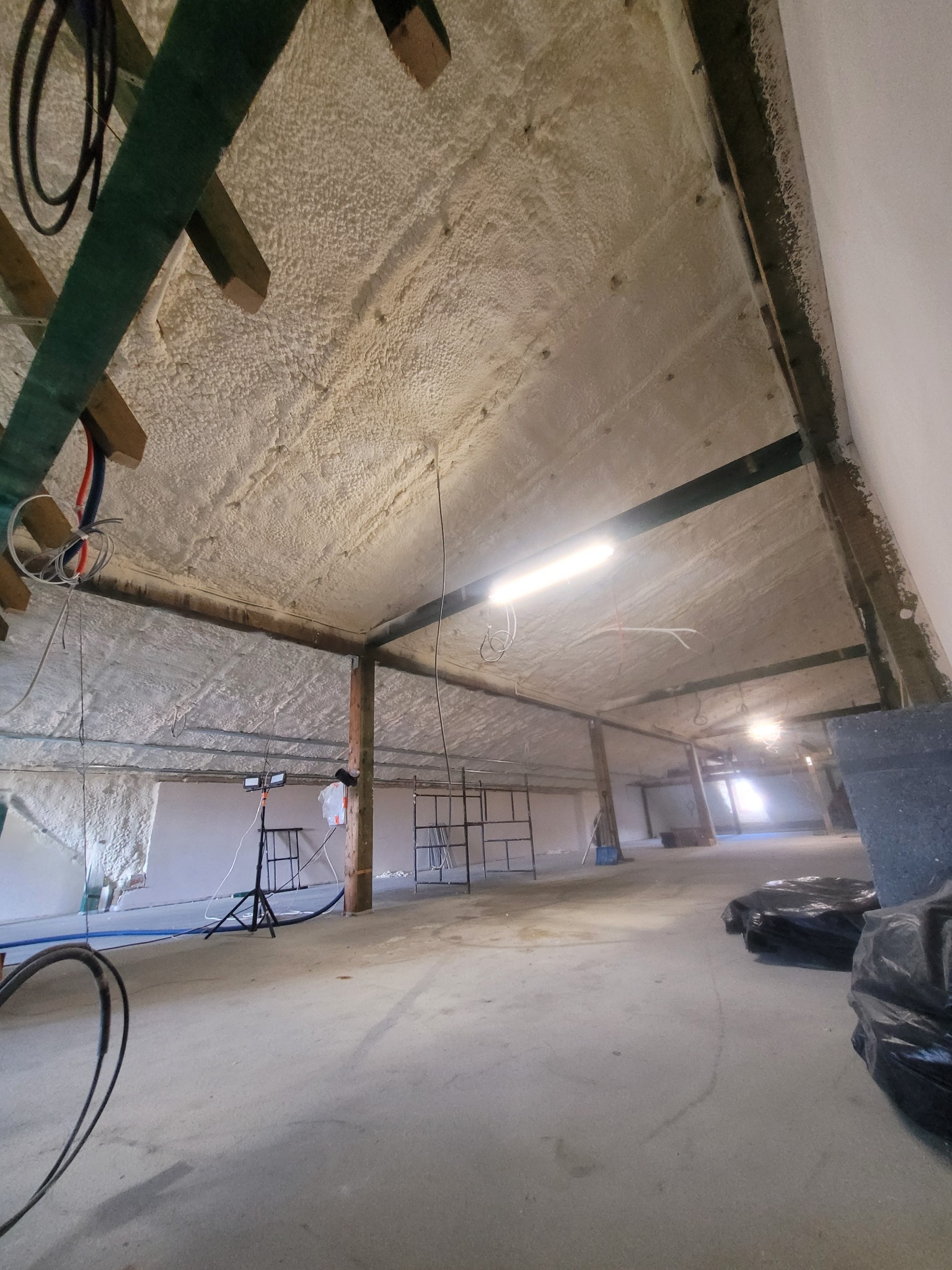 Ocieplone poddasze pianą z widocznymi elementami konstrukcyjnymi, oświetleniem i sprzętem. Realizacja ocieplenia w surowym wnętrzu.