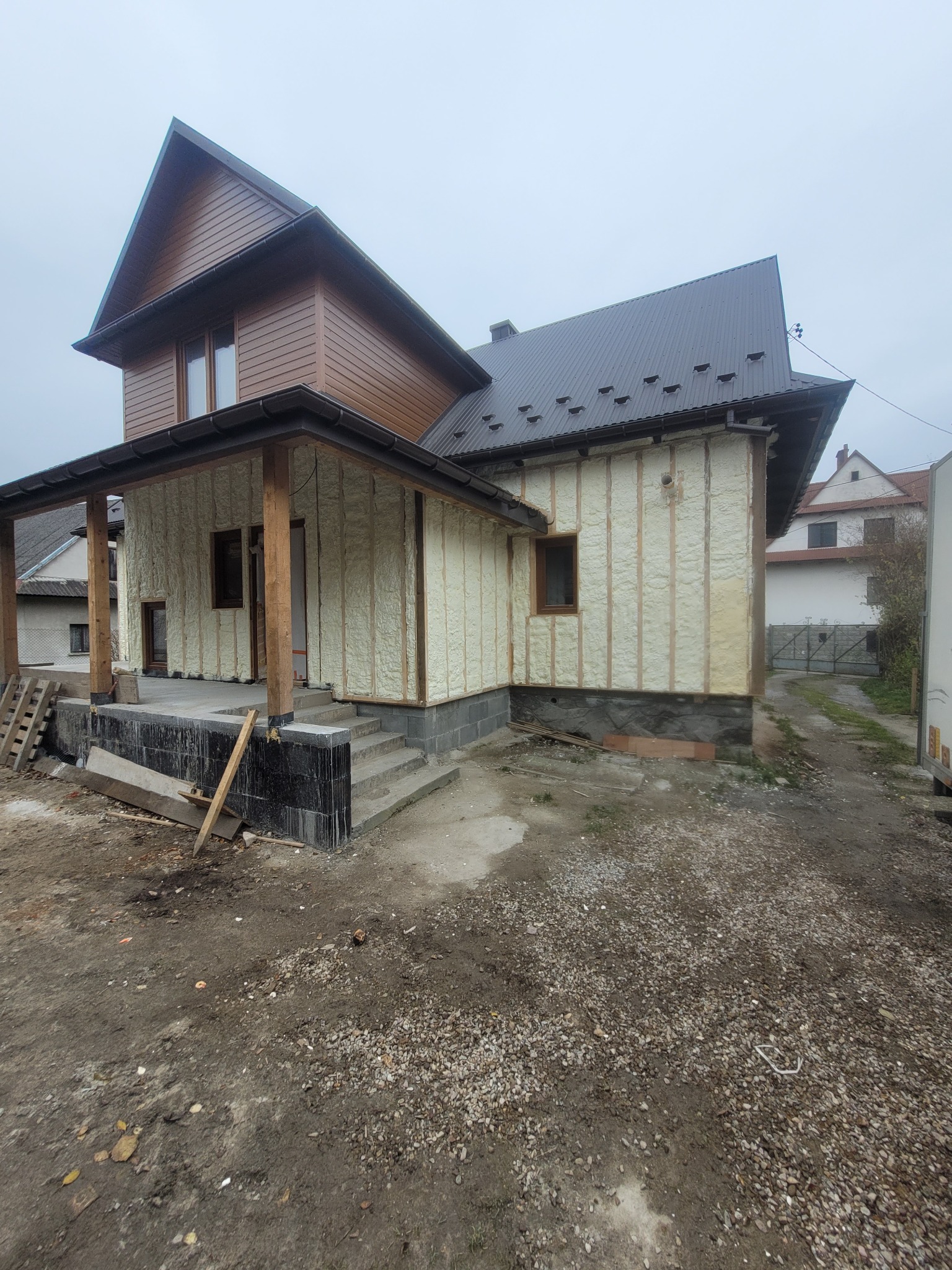 Dom w trakcie ocieplania: widoczne drewniane ramy i wypełnienie pianką na ścianach. Częściowo wykończona elewacja, teren wokół w trakcie prac ziemnych.