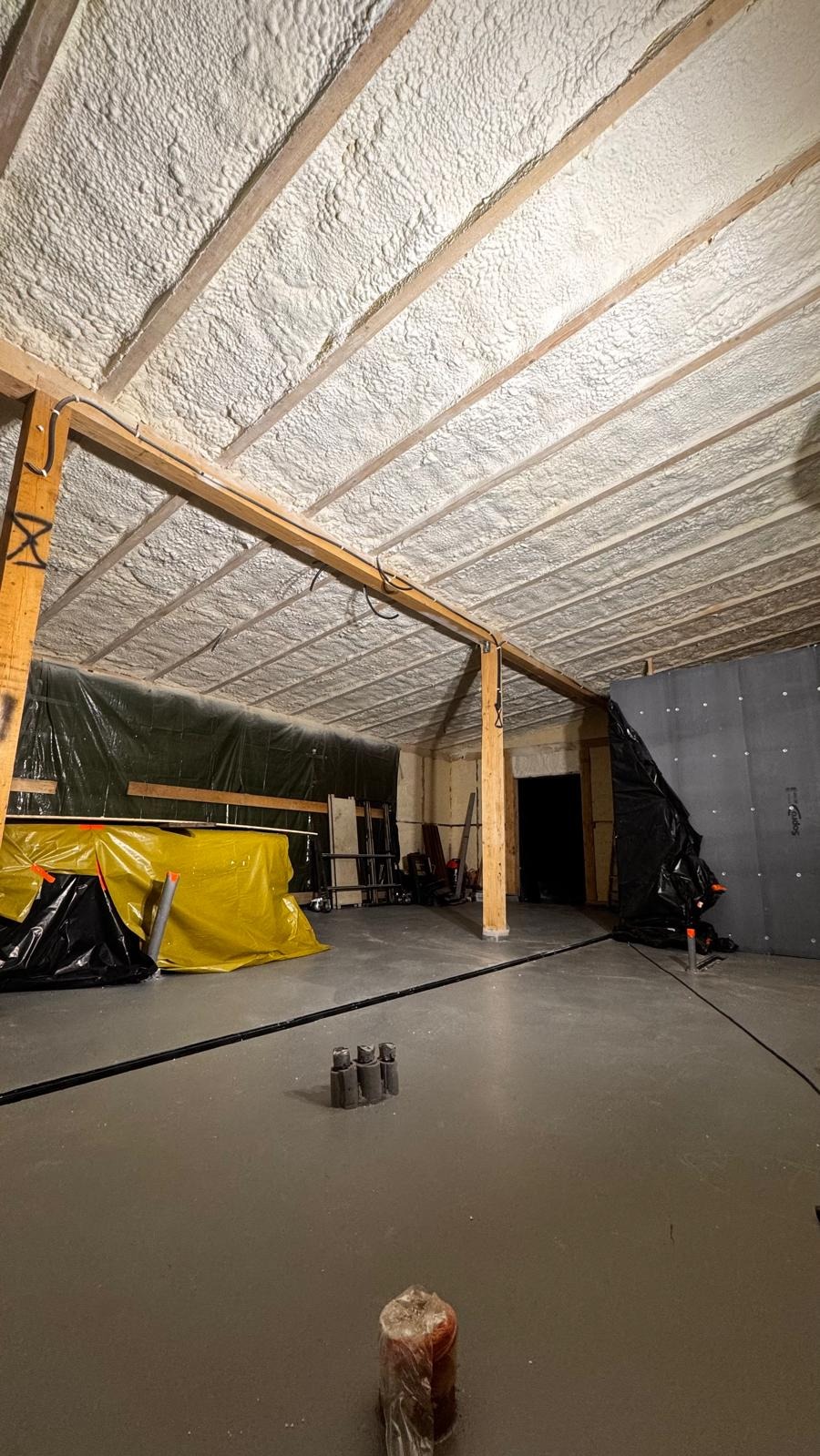 Sufit poddasza po natrysku izolacji piankowej PUR, widoczne drewniane belki konstrukcyjne i równomierna warstwa piany. Na podłodze zabezpieczenia i narzędzia.