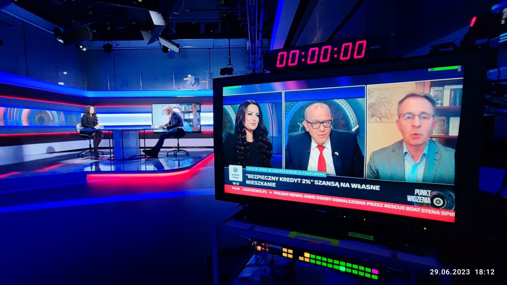 Studio telewizyjne z gośćmi omawiającymi temat bezpiecznego kredytu na mieszkanie, widoczne na monitorze podczas nagrania.