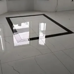 Błyszcząca, biała podłoga z płytek z czarną ramą dekoracyjną w nowym, jasnym pomieszczeniu. Widoczne dwa okna z parapetami.