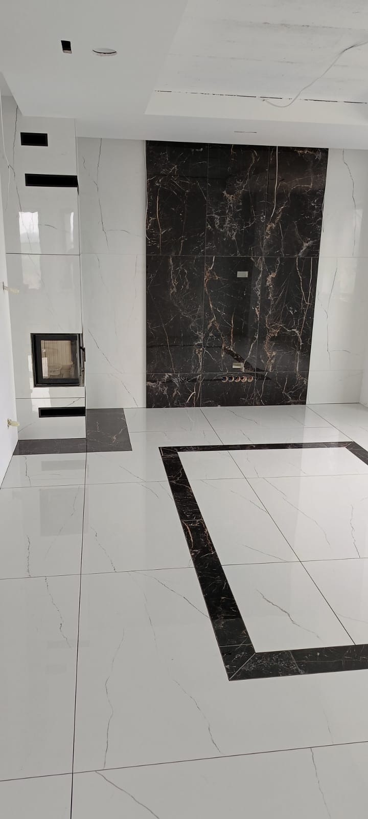 Wykończona łazienka z białymi płytkami imitującymi marmur, czarnymi akcentami i wbudowanym kominkiem.