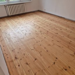 Darfloor - Jasna, odnowiona podłoga z desek sosnowych w pustym pokoju z białymi ścianami i grzejnikiem żeberkowym pod oknem.