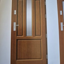 Darfloor - Brązowe drzwi wejściowe z panelem ze szkła matowego, widoczne na stronie katalogu z nazwą 'MARIUSZ' i kodem QR w dolnym rogu.