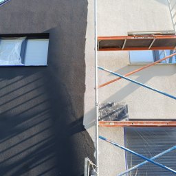 Darfloor - Elewacja domu w trakcie malowania, widoczne rusztowanie, okno zabezpieczone folią, część ściany w kolorze grafitowym, druga część w jasnym odcieniu.