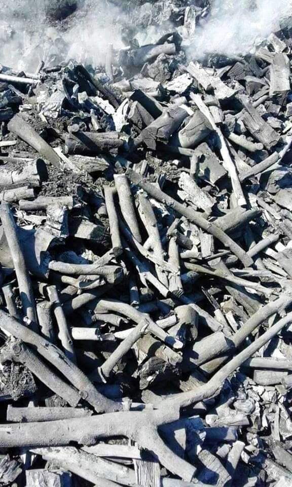 Stos czarnego opału z widocznymi fragmentami drewna i dymem w tle.