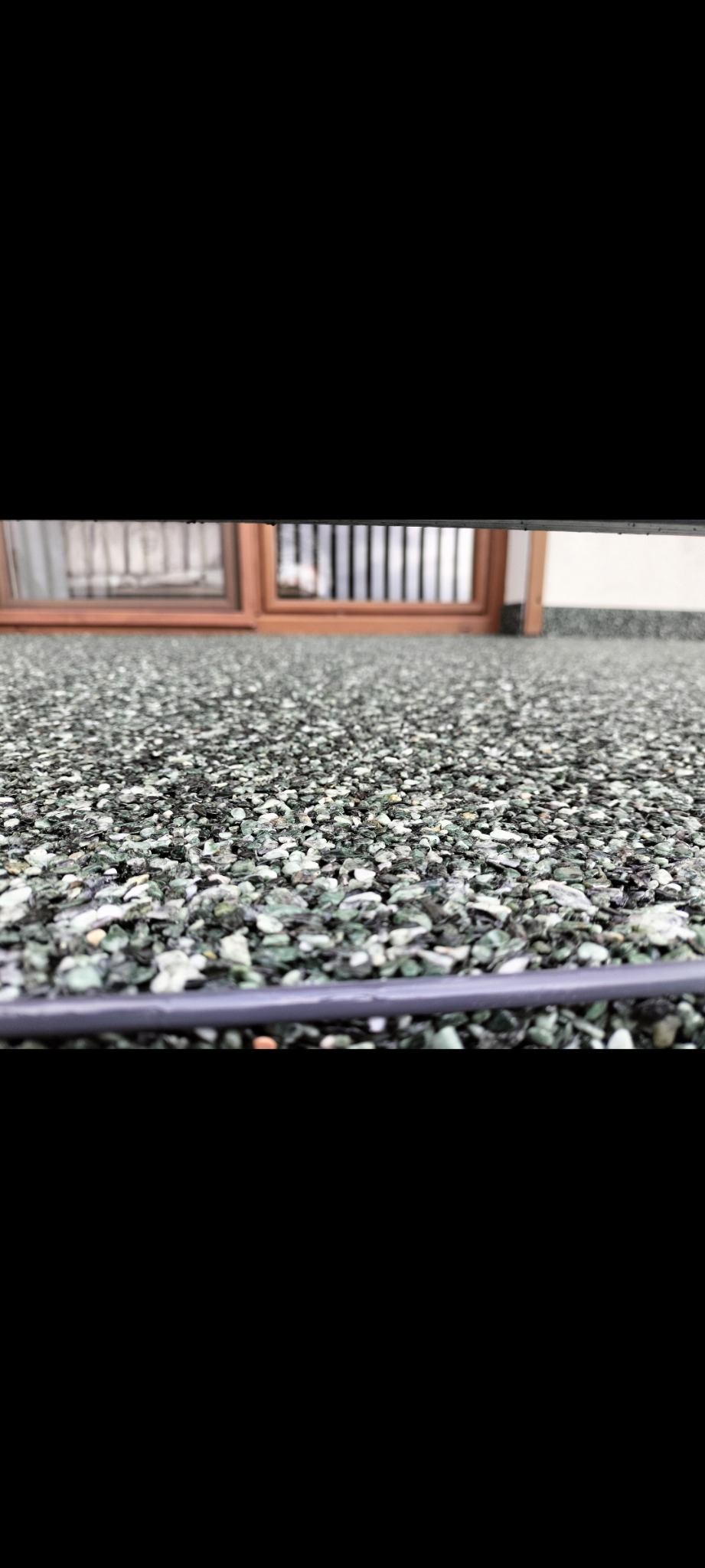 Szara posadzka żywiczna z drobnymi kamyczkami, widok z niskiego kąta, na tle okno z drewnianą ramą i metalowymi szprosami.